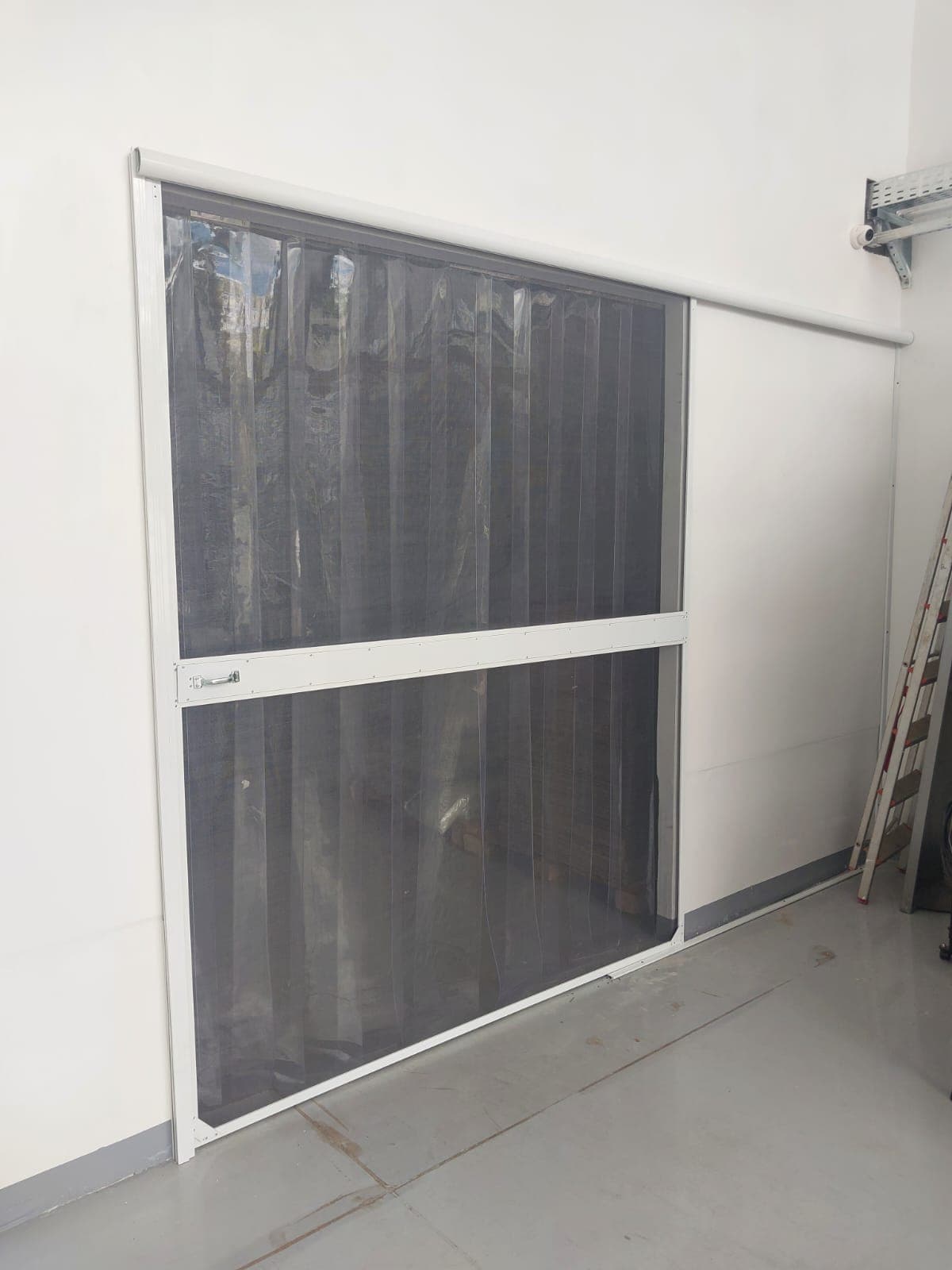 Cortina de tela mosquiteira com faixas de PVC transparente instalada em vão de acesso de galpão