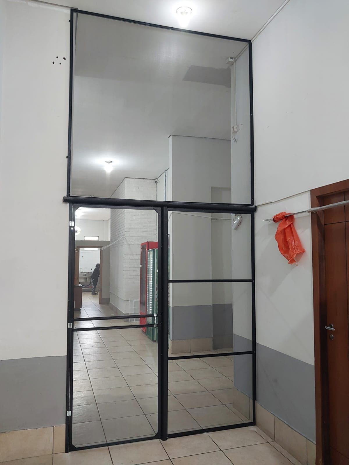 Porta e painel de tela mosquiteira com perfil preto instalados em corredor de estabelecimento comercial