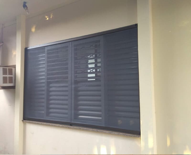 Janela veneziana de três folhas protegida por tela mosquiteira de perfil preto instalada por fora, em varanda de casa